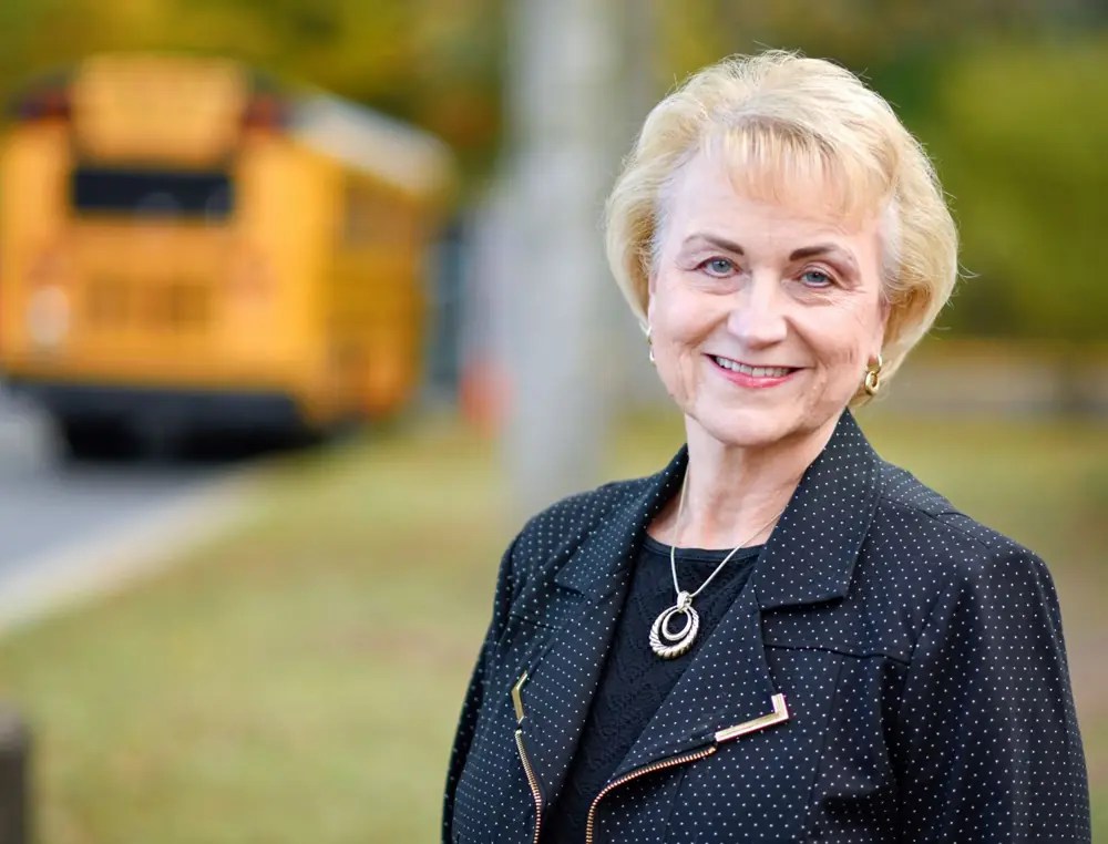 Debbie Kilpatrick smiling, with a yellow school bus in the background
