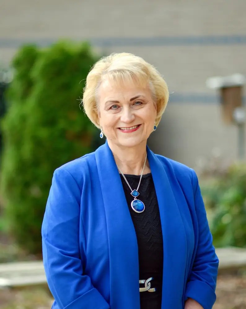 Debbie Kilpatrick smiling, wearing a royal blue jacket, outside a school